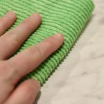 hand cleaning white countertop with green rag