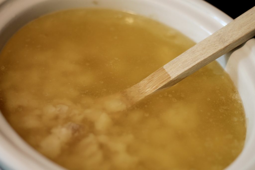 Beef tallow rendering in a crock pot with a wooden spoon