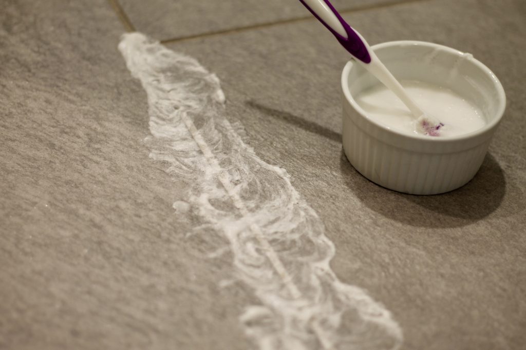 Homemade Grout Cleaner being applied with a toothbrush on gray tile floors